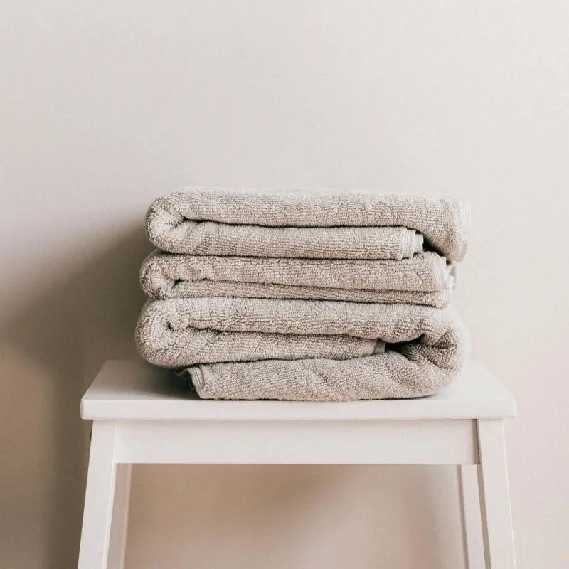 Pila de toallas gris claro apoyadas sobre un taburete blanco_Algodonea Textil