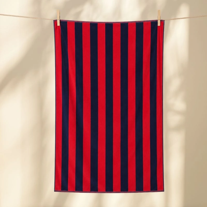 Toalla de playa rayas azul marino y rojo tendida al sol sobre una pared amarilla - Algodonea textiles portugueses